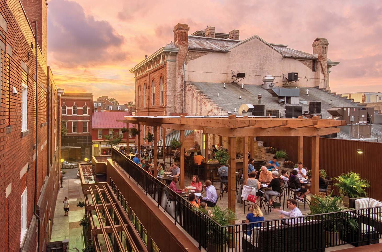 Rooftop bar dining area nestled at the edge of two buildings with a sunset in the distance